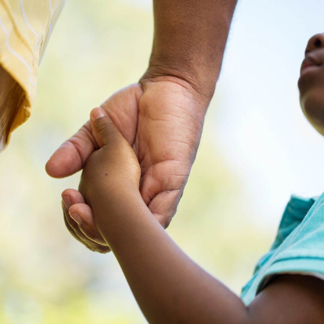 Father holding child's hand indicating successful co-parenting in summer in Texas.