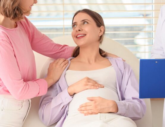 A same-sex couple one showing support to the other lying on a chair pregnant.